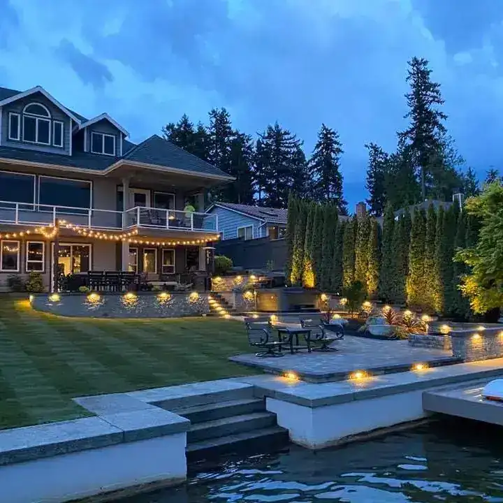 An Archterra paver patio at dusk, string-lit, on a lakefront property