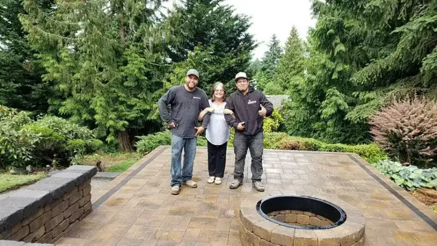 Two Archterra crew members with a customer on a finished paver patio with a fire pit